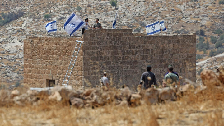 Des colons israéliens hissent des drapeaux sur une maison palestinienne qu'ils ont saisie, à Beit Sahur, au sud de Bethléem, en Cisjordanie occupée, le 14 août 2026