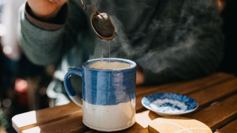 Unidentified person lifts a tea strainer out of a piping hot blue and white mug of tea.