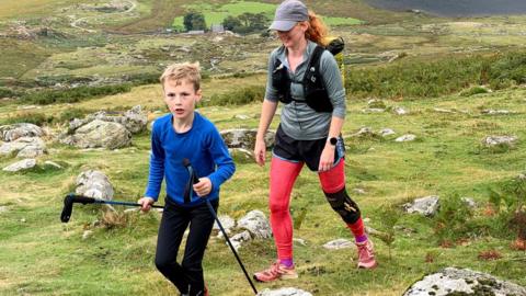  A little boy running with poles, a woman is behind him