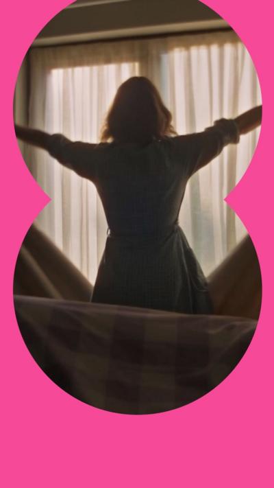 A woman silhouetted in front of a window as she throws the curtains open.