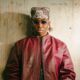 FOLA wearing a maroon leather bomber jacket, sunglasses, and headscarf