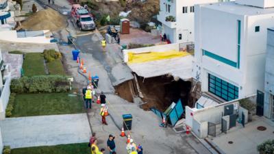 Debris and warped road pictured in front of sinkhole beside white house in Malibu