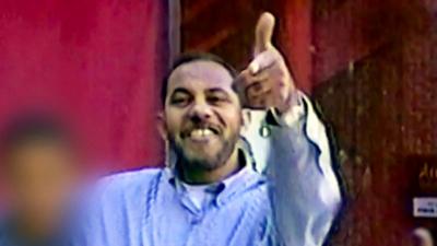 Omar al-Bayoumi in a blue shirt appears to make a gun sign with his hand