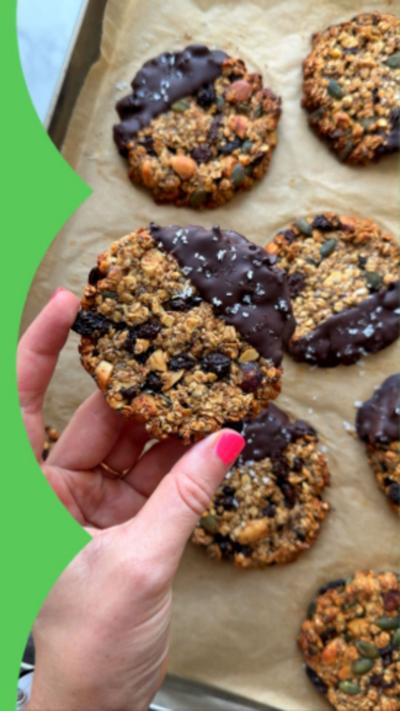 A tray of homemade granola cookies dipped in chocolate with sea salt flakes. A hand reaches in from the left and is holding one of the cookies