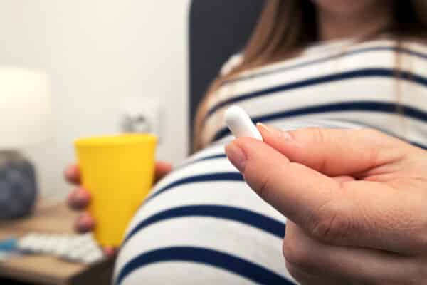 The pills in the pregnant woman's hand sitting on the bed