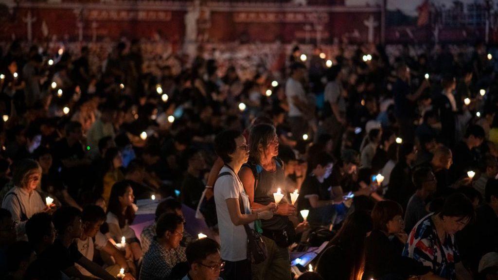 A crowd gathers at night, with many people holding candles