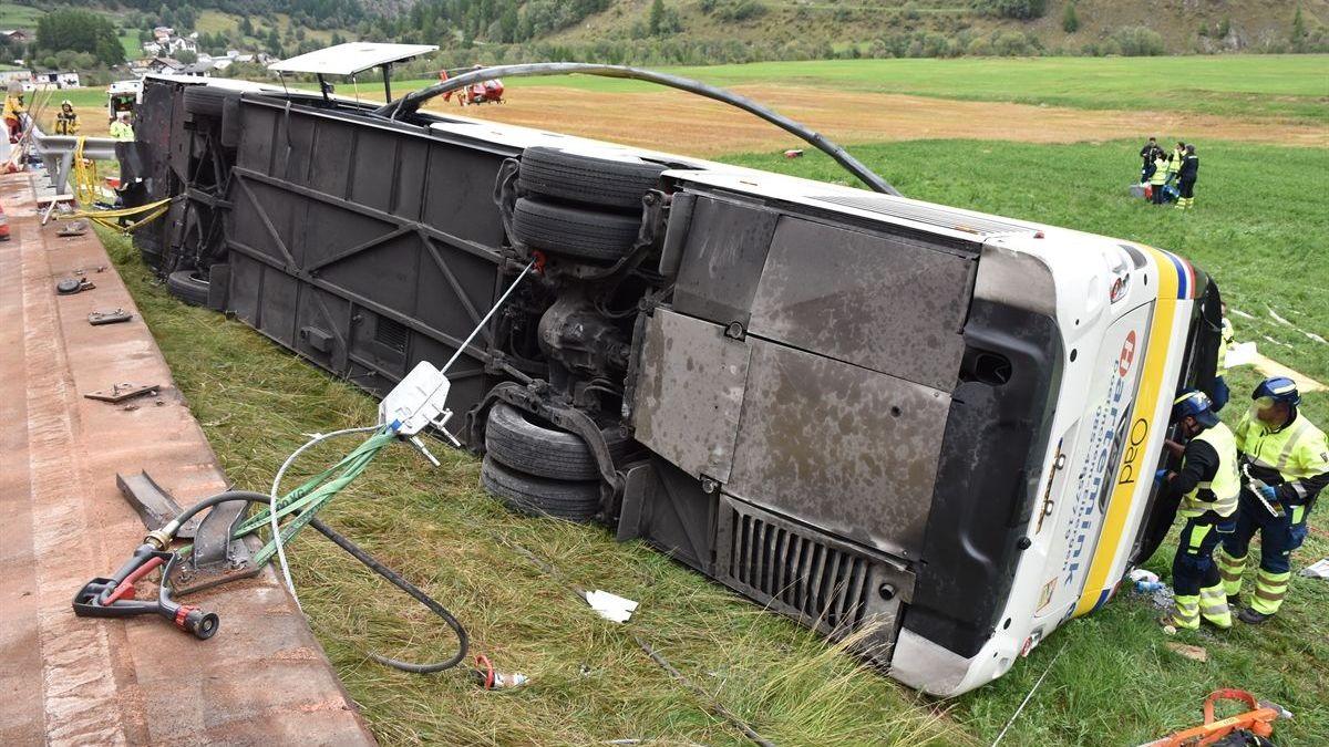 A police photo show a coach on its side on a grassy verge as rescue workers peer through its windows
