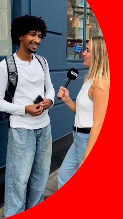 A woman holding a microphone speaks to a man