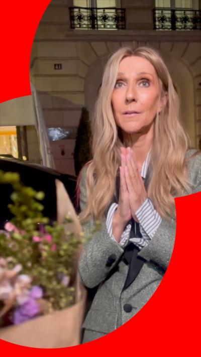 Celine Dion, in a grey suit, makes a thank you hand gesture when she is offered flowers by a fan.