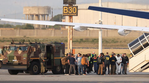 Des agents du FBI interviennent sur le tarmac de l'aéroport international du Cap dans le cadre de la procédure d'extradition de ressortissants nigérians soupçonnés d'appartenir au réseau criminel organisé « Black Axe », au Cap, en Afrique du Sud, le 11 septembre 2026.