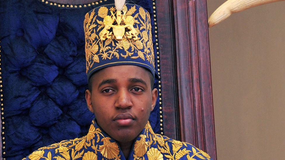King Oyo pictured at 18 during his coronation wearing a gold embroidered jacket and hat.