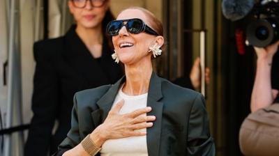 Celine Dion with a hand over her chest coming out of her hotel.