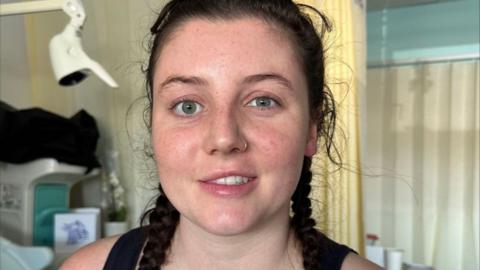 Niamh Foster pictured in hospital with dark hair in braids. One eye appears more open than the other, and her lips are at different heights on each side. 