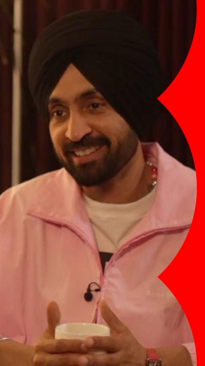 Diljit Dosanjh sitting down in a pink jacket holding a mug.