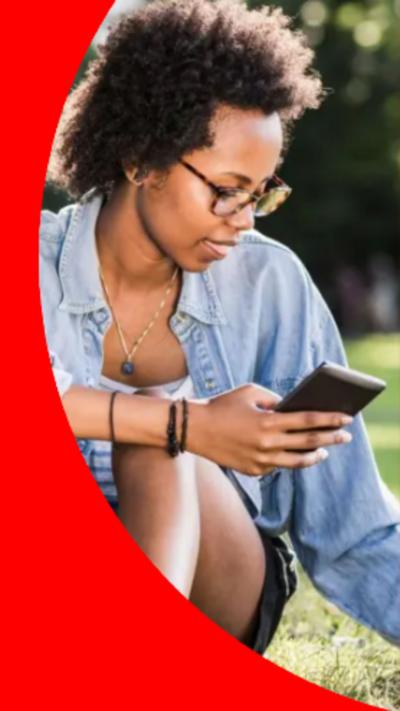 A young woman sat on the grass holding her mobile phone. Her tablet is on the ground in front of her.