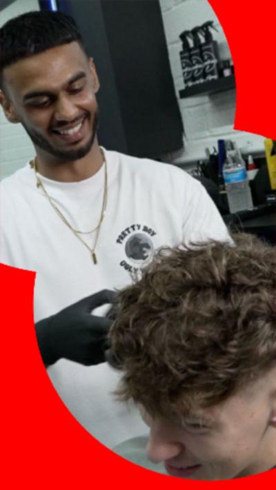 Young barber with short dark hair cutting somebody's hair.