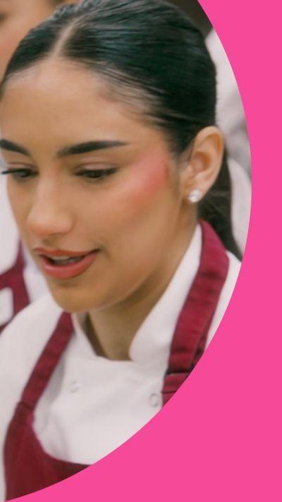 A woman with long dark hair tied back is wearing chef's whites under a red apron.
