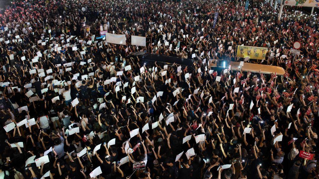 A crowd gathers in the night, raising banners