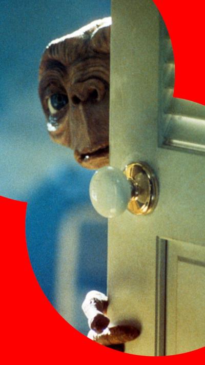 A still of E.T. peering around a white cupboard door.
