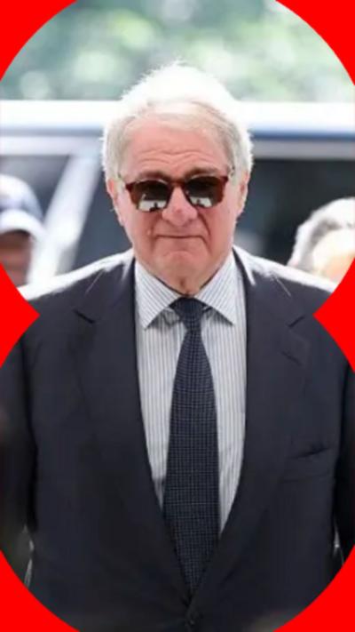 A man with short grey hair wearing sunglasses and a dark suit