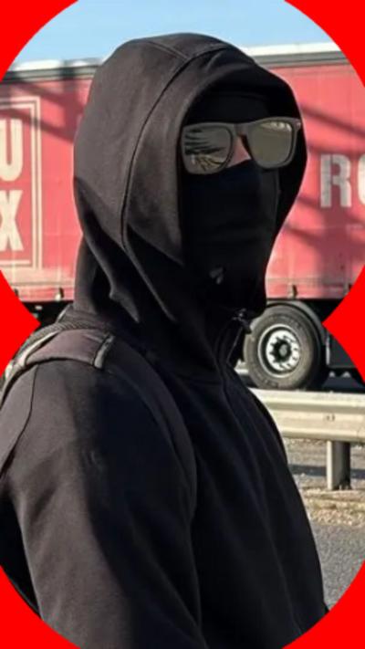 A person dressed in all-black clothing, wearing sunglasses and a balaclava. They also have their hug over their head.