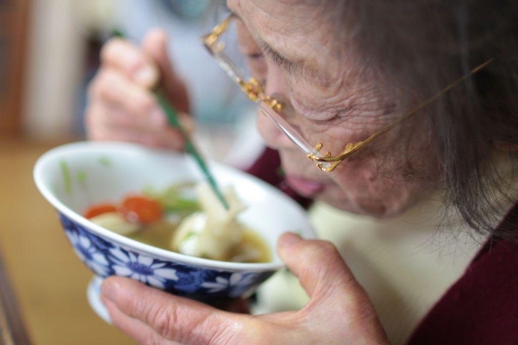 A close image of an elderly Japanese woman eating noodle soup 