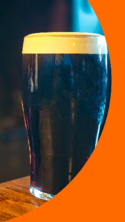 Close up of a pint of ale on a wooden table, with a roaring fireplace in the background.