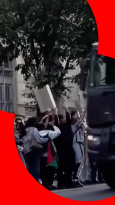 A number of students protesting as a police van drives past.