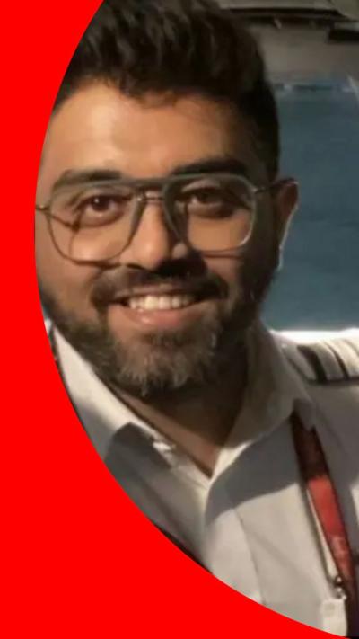 A man with short dark hair and a short beard wearing glasses and a white shirt smiles at the camera