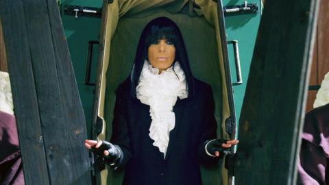 Claudia Winkleman emerging from a coffin