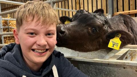 Smiling teenage boy with blond hair next to a black calf