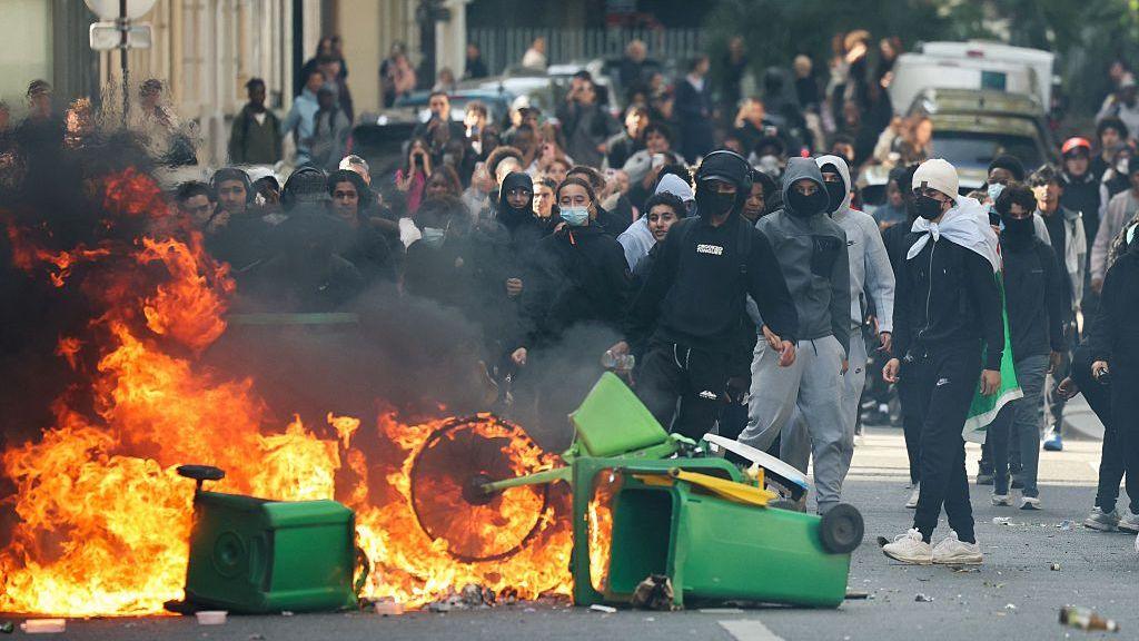 A student sets fire to rubbish bins as protesting students carry out blockading action near place de la Nation, in Paris, on October 2, 2026. Since late September, students have staged protests outside schools over grievances ranging from timetables, class sizes and a shortage of teachers to overheated classrooms during this year's heatwaves. The protests started in the Ile-de-France region around Paris but have now spread to other cities nationwide.