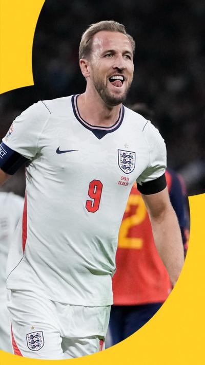 England captain Harry Kane celebrating a goal. He is wearing a white England home shirt.