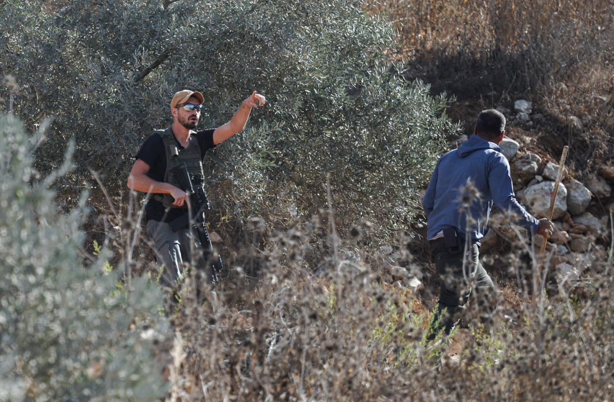 gestures for a Palestinian farmer to leave while holding a rifle as Palestinians are forced out of their olive groves during the harvest season in the village of Beita near Nablus, in the Israeli-occupied West Bank, October 2, 2026. REUTERS/Ammar Awad