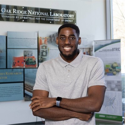 Stanford PhD student Obi Nnorom stands in front of a sign for Oak Ridge National Laboratory.