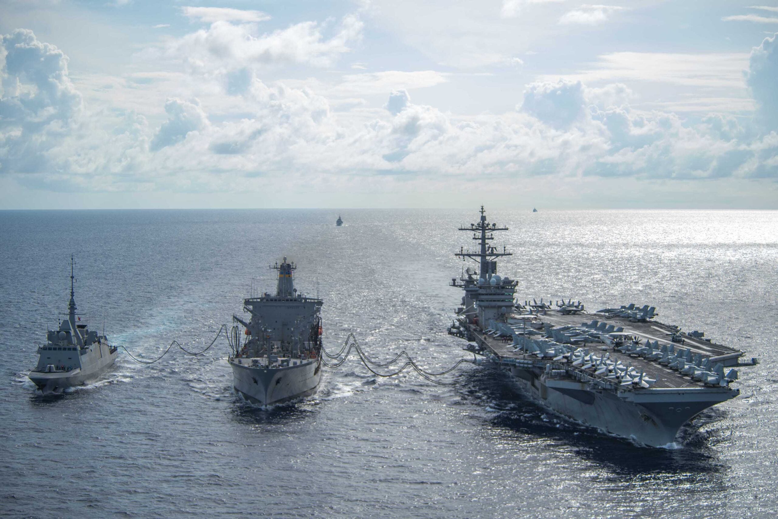 US Navy oiler USNS Big Horn replenishing an aircraft carrier at sea under a cloudy sky