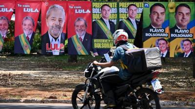 Flags and towels bearing the images of Brazil's President and presidential candidate Luiz Inacio Lula da Silva and right-wing senator and presidential candidate Flavio Bolsonaro are displayed for sale on a street in Brasilia as someone on a motorcycle drives by.