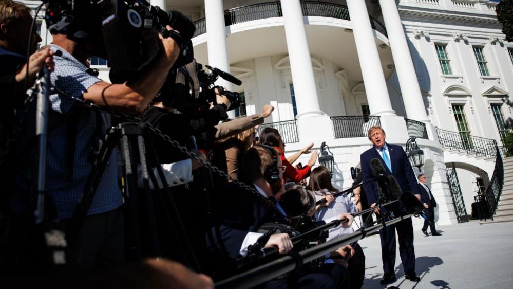 Photographers and television crews crowd the foreground as Donald Trump  speaks outside the White House