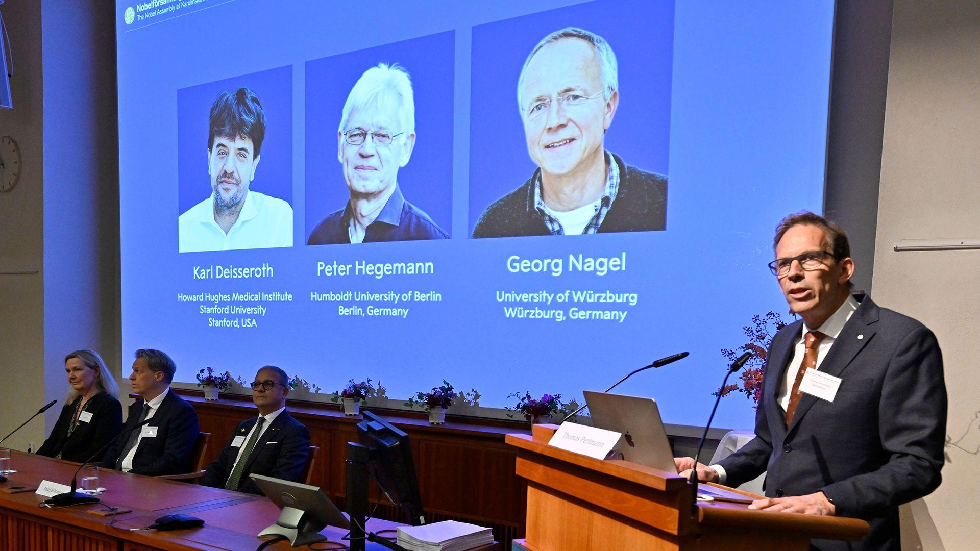 Nobel Committee Secretary General Thomas Perlmann (R) speaks to the media in front of a screen displaying the names of this year's laureates (L-R) Karl Deisseroth, Peter Hegemann and Georg Nagel during the announcement of the winners of the 2026 Nobel Prize in Physiology or Medicine at the Karolinska Institute in Stockholm, Sweden, on October 5, 2026. 