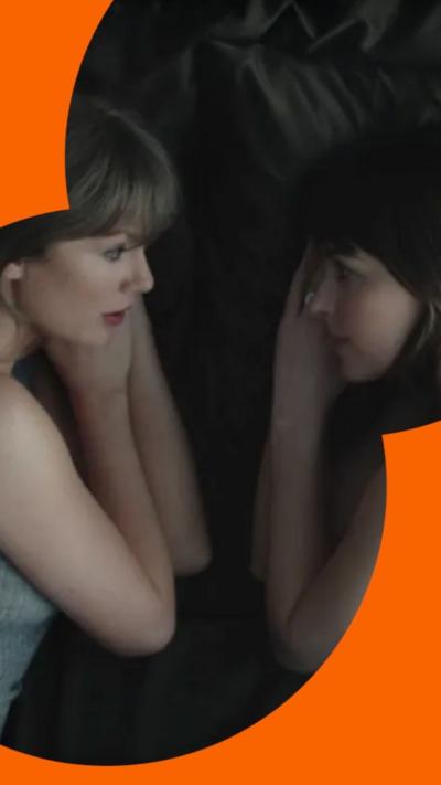 Taylor Swift and Dakota Johnson lay in bed facing each other looking at each other with their hands resting under their faces.