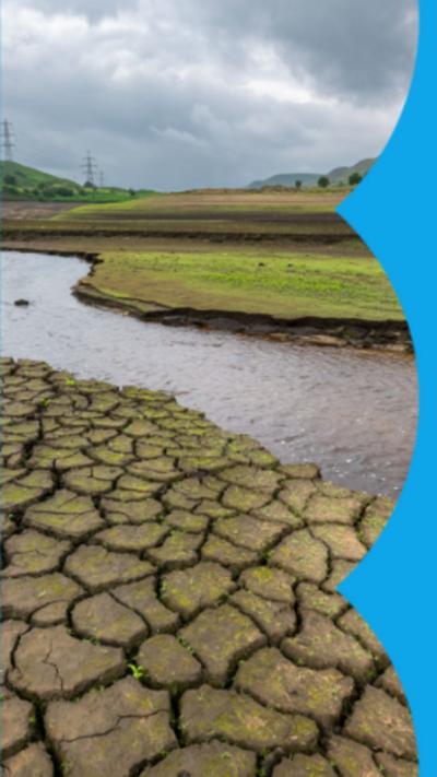 An image of drought affected ground alongside a water stream, with green hills in the background.