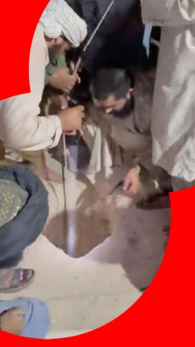 A number of men crouch over a well with a line and torch looking down.