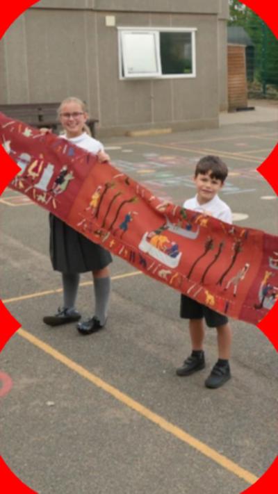 School teachers and students stand in a line holding out copy of Bayeux Tapestry