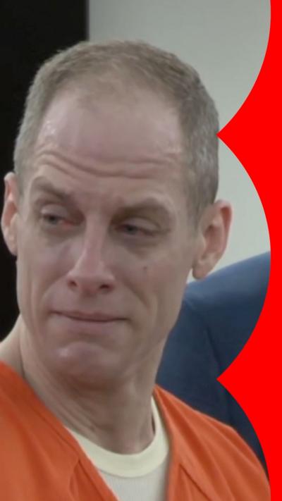 Caleb Flynn has short grey hair. He is wearing a white T-shirt and orange prison overalls.