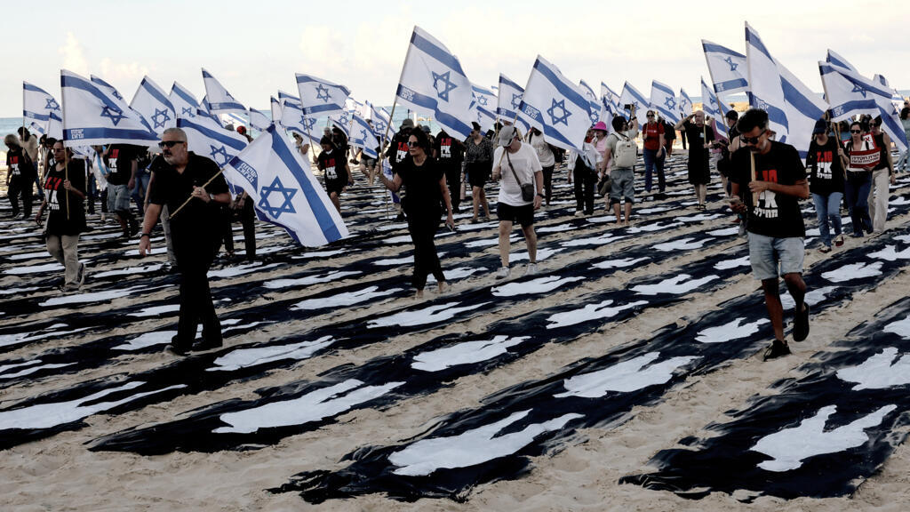 People carrying Israeli flags walk through a commemorative installation set up on the beach in Tel Aviv to mark the third anniversary of Hamas's October 7 attack on Israel.
