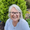 Ellen Allen is photographed outdoors. She is wearing glasses and smiling.