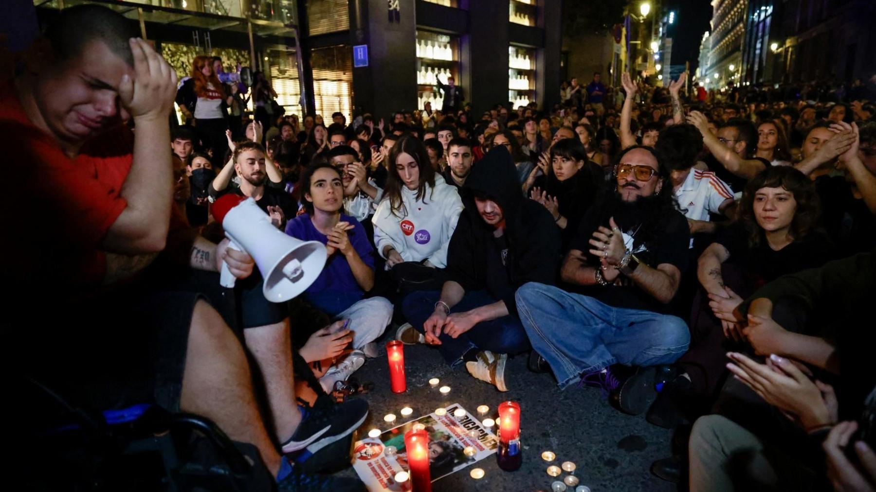 People gather in one of Madrid's main squares, Puerta del Sol,  following the death of Maricarmen Abascal. One man can be seen carrying a megaphone as he appears emotional, while others sit crossed legged. Candles have been lit in memory of Maricarmen. 