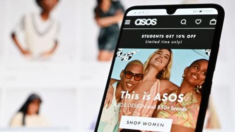 A laptop screen and mobile phone shows the website of online fashion retailer ASOS on August 12, 2021. (