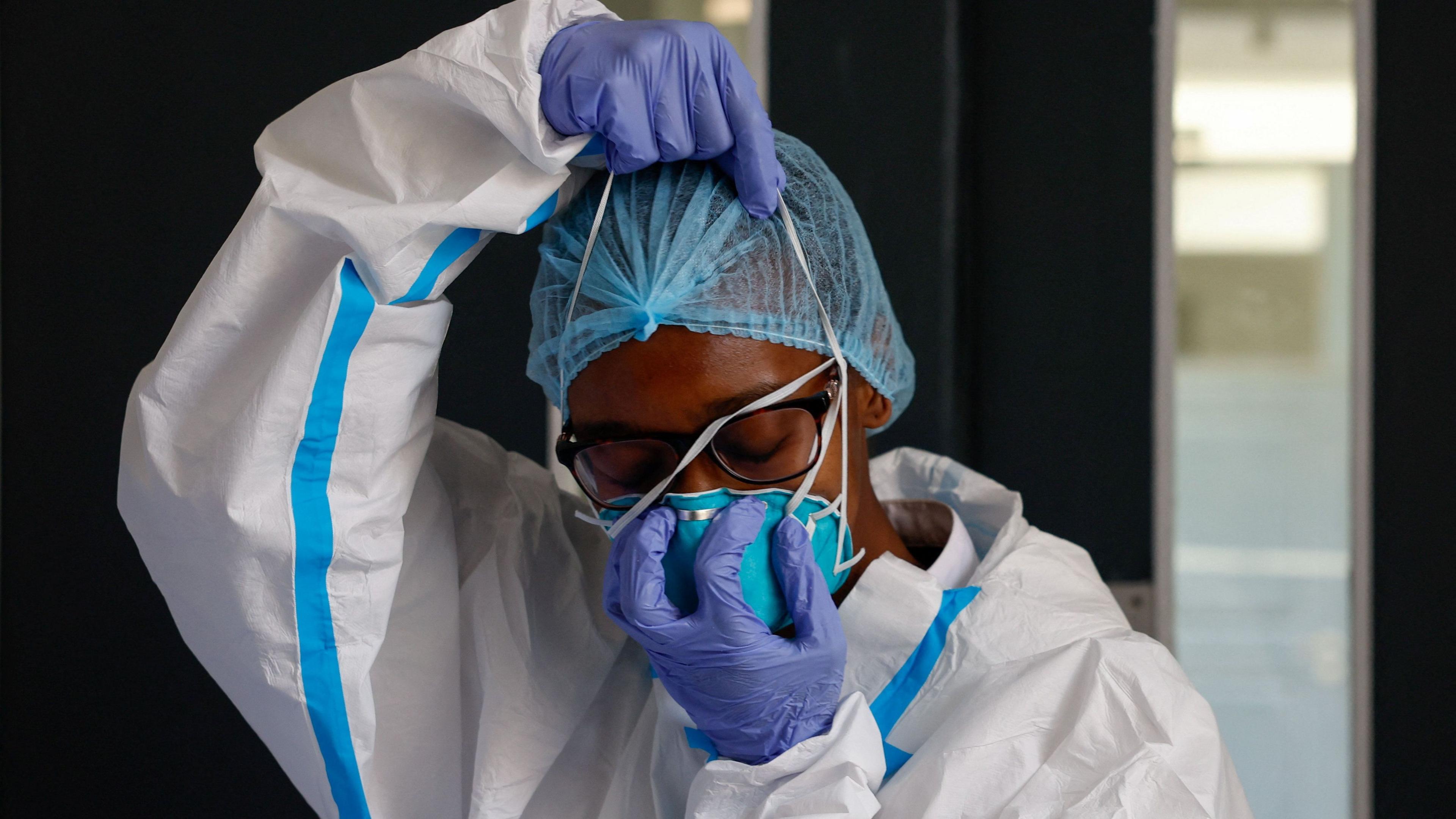 A nurse wears in white protective clothes and blue gloves, wears a face mask