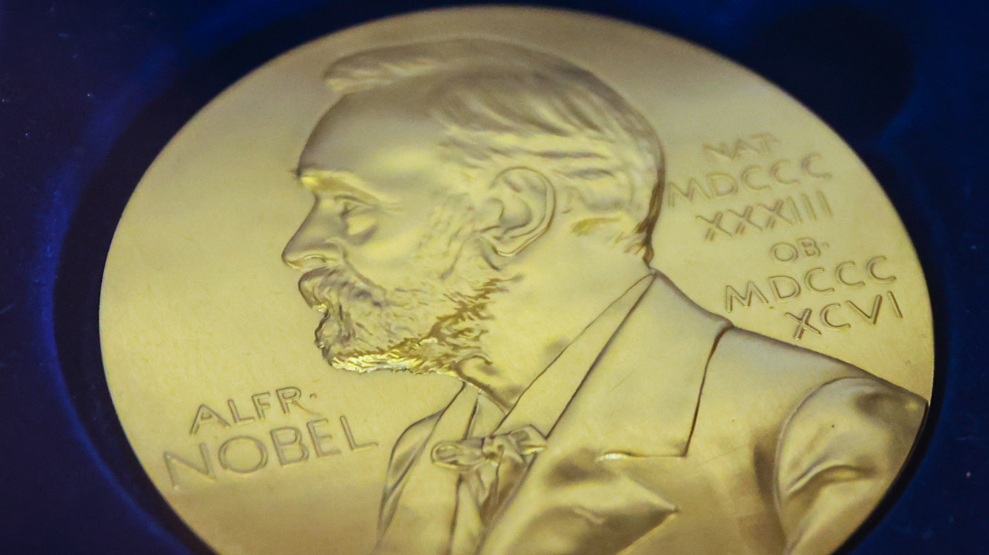 Gold medal in blue background with a picture of Nobel sketched out of the coin and roman numerals on the right. 